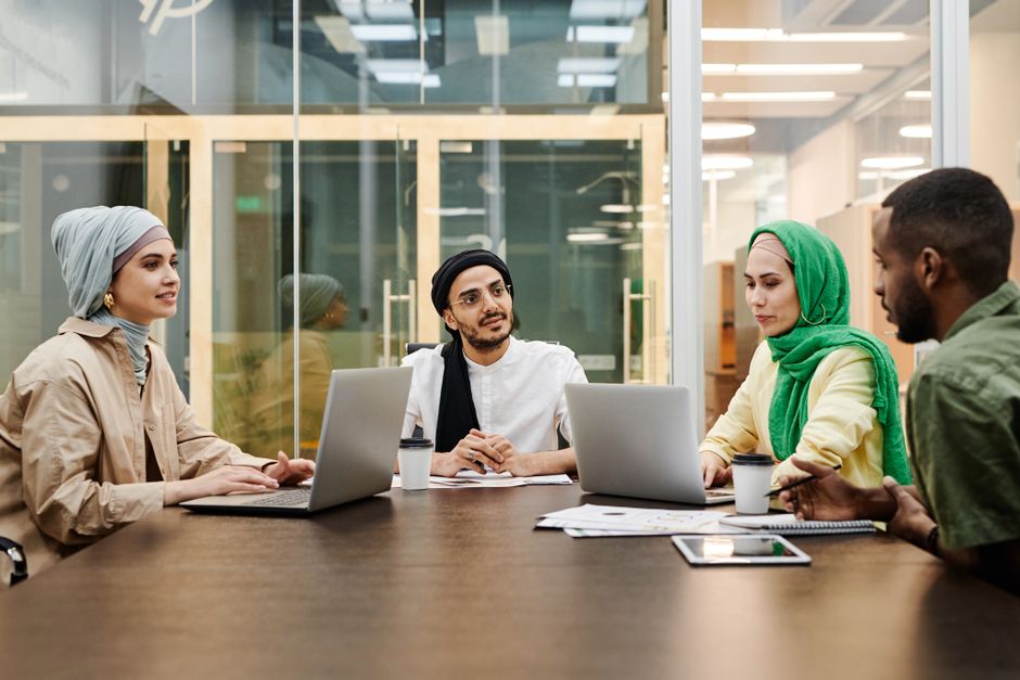 A diverse group discussing ideas in a modern office setting, using laptops and tablets.